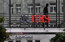n employee of multinational investment bank UBS walks past a sign of Swiss giant banking UBS above a sign of Credit Suisse in Zurich on August 31, 2023.