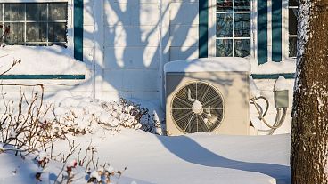 A heat pump unit on the side of a home in winter.