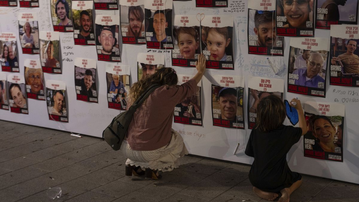 A woman touches photos of Israelis missing and held captive in Gaza, displayed on a wall in Tel Aviv