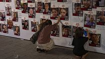 Eine Frau berührt Fotos von Israelis, die in Gaza vermisst und gefangen gehalten werden, die an einer Wand in Tel Aviv ausgestellt sind.
