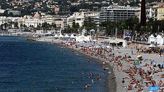 Nicht viel Schnee: Menschen sonnen sich und schwimmen am langen Kieselstrand von Carras im Zentrum von Nizza an der Côte d'Azur