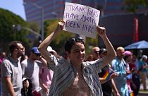 An LGBTQ+ activist holds a sign reading 'Trans Folks Have Always Been Here' in April