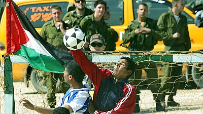FILE: Israeli soldiers, background, watch as Palestinians and foreign activists play at the construction site of Israel's separation barrier in the village of Bil'in. 