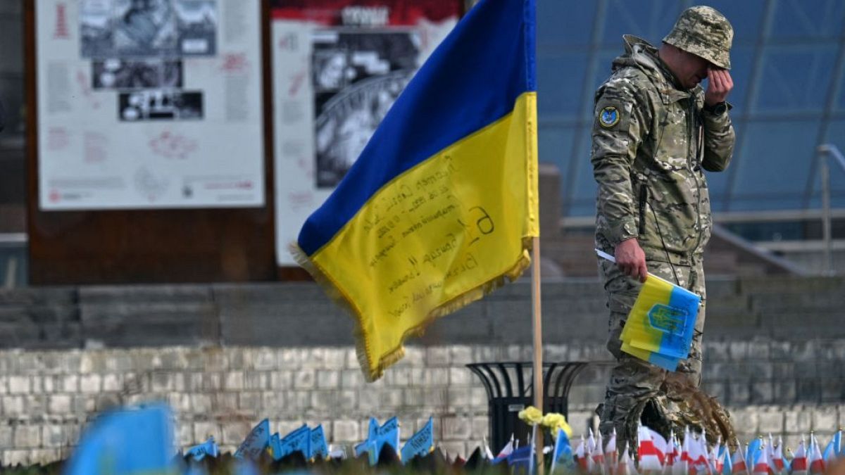 A serviceman mourns next to a Ukrainian flag at a makeshift memorial for fallen soldiers at Independence Square in Kyiv