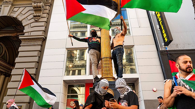 Pro-Palestinian supporters climb a clock during a demonstration against the APEC Summit