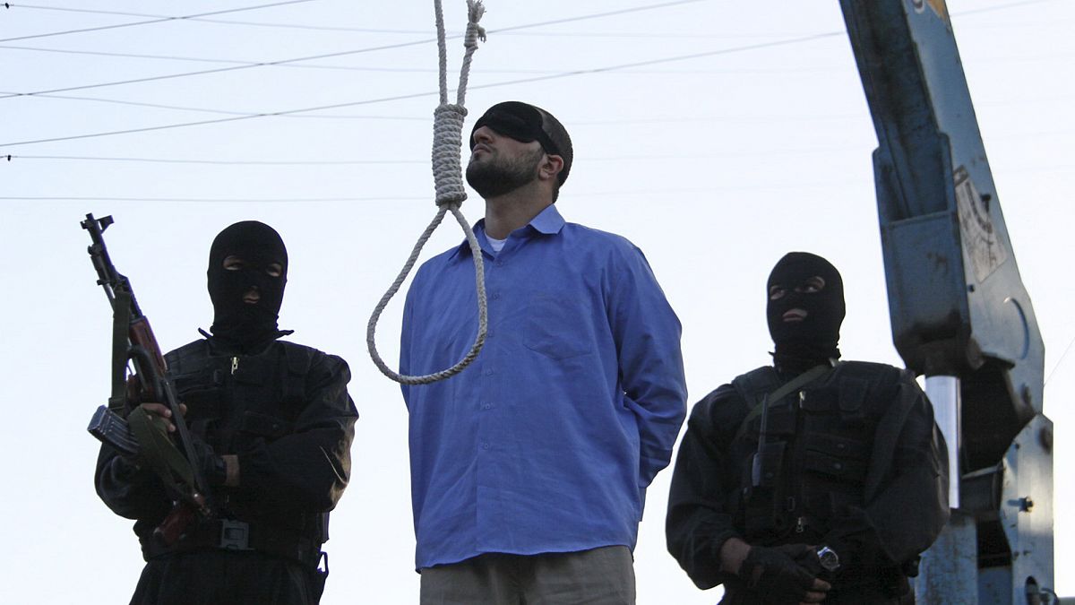 رجل معصوب العينين أدين بالسطو المسلح واختطاف وقتل شرطيين، بما في ذلك رئيس شرطة شيراز، ينتظر شنقه علنًا، بينما ينظر اثنان من ضباط الشرطة في مدينة شيراز، إيران،16 أبريل 2011