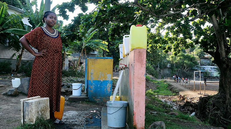 A woman waits for her bucket to be full at a water point in M'tsamoudou, near Bandrele, on the French Indian Ocean territory of Mayotte, 21 October 2023.