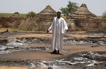 قروي سوداني من قرية أم هشاب، في ولاية شمال دارفور السودانية يقف أمام كوخه المحترق (أرشيف). 2004/08/29
