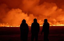 People watch as the night sky is illuminated caused by the eruption of a volcano in Grindavik on Iceland's Reykjanes Peninsula, 18 December 2023. 