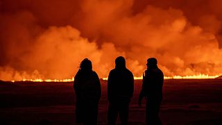 People watch as the night sky is illuminated caused by the eruption of a volcano in Grindavik on Iceland's Reykjanes Peninsula, 18 December 2023. 