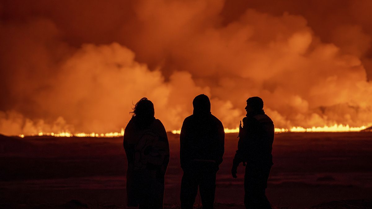 Des personnes observent l'illumination du ciel nocturne causée par l'éruption d'un volcan à Grindavík, sur la péninsule de Reykjanes, en Islande, le 18 décembre 2023. 