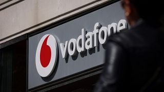 A Lady walks by a Vodafone shop with the company logo on display