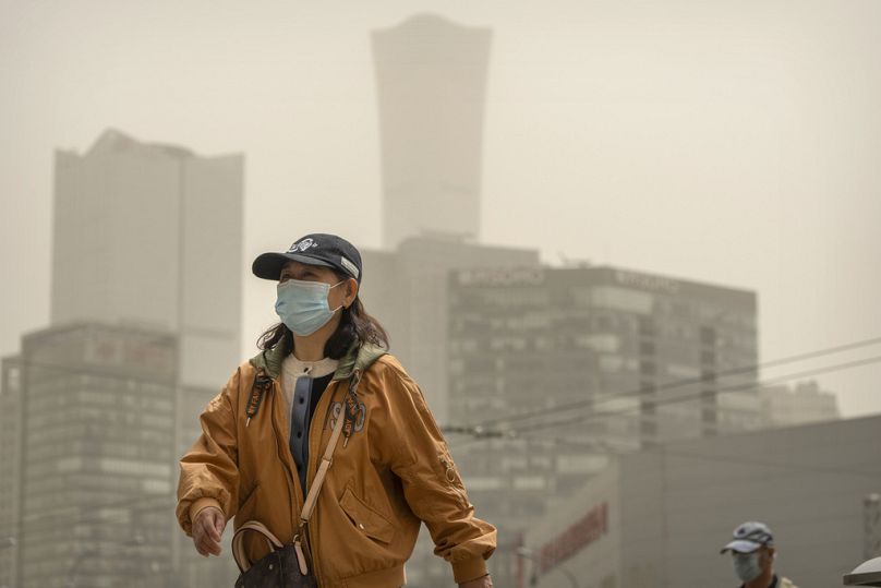 A woman wearing a face mask walks across an intersection during a dust and sandstorm in Beijing, Tuesday, April 25, 2023.