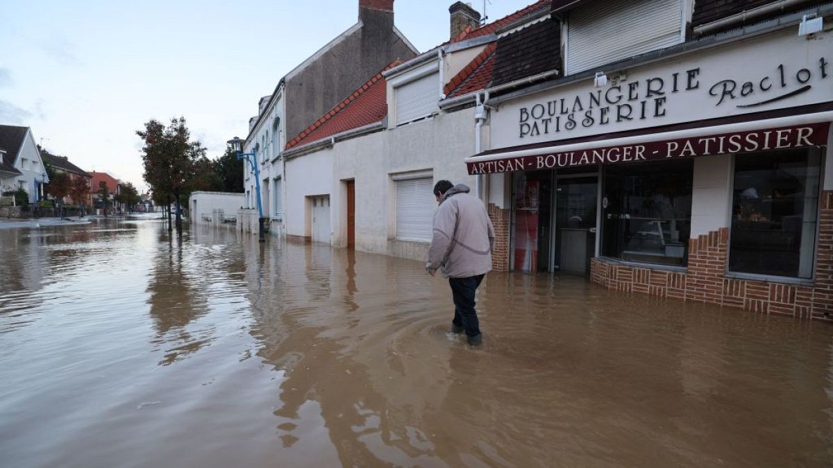 A pedestrian walks past a bakery in a flooded street in Saint-Etienne-au-Mont, Pas-de-Calais on Wednesday
