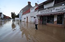 A pedestrian walks past a bakery in a flooded street in Saint-Etienne-au-Mont, Pas-de-Calais on Wednesday