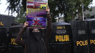 Жена държи афиш по време на протест против английската група Coldplay преди концерта й в Джакарта, Индонезия 