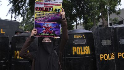 A woman holds a poster during a rally against British band Coldplay ahead of its concert in Jakarta, Indonesia