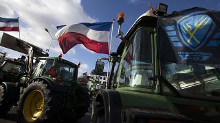 The Farmers Defense Force flag, right, and Dutch flags, fly in the wind on an intersection blocked by tractors in The Hague, Netherlands, Wednesday, Feb. 19, 2020.