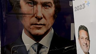 The image of presidential hopeful Javier Milei fills the side of a bus carrying his supporters, parked by a wall where a sign promotes his rival Sergio Massa, in Buenos Aires