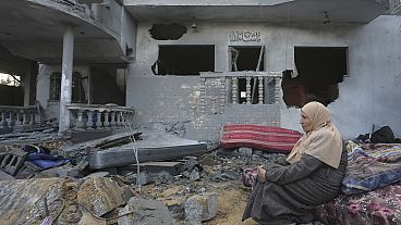 Eine palästinensische Frau sitzt am Montag, 20. November 2023, in Rafah neben Häusern, die durch die israelische Bombardierung des Gazastreifens zerstört wurden. 