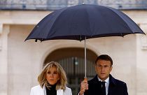 امانوئل ماکرون، رئیس جمهور فرانسه، در حالی که با همسرش بریژیت ماکرون راه می رود، چتر در دست گرفته است.