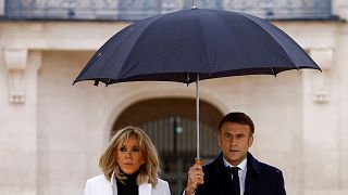 امانوئل ماکرون، رئیس جمهور فرانسه، در حالی که با همسرش بریژیت ماکرون راه می رود، چتر در دست گرفته است.