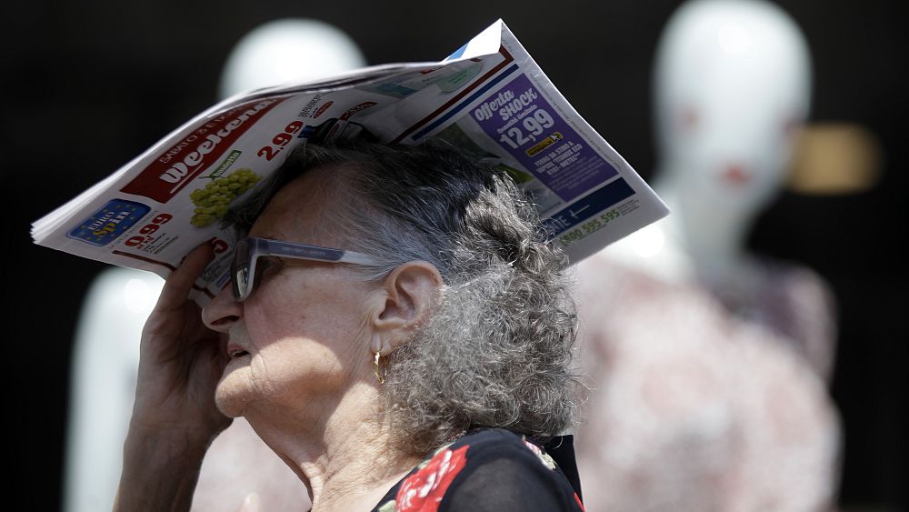 Възрастна жена се крие от горещото слънце с вестник в