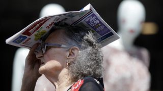 Una donna anziana si ripara dal sole cocente con un giornale, a Milano, Italia.