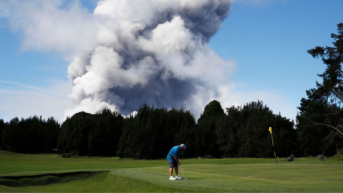 A man plays gold in Hawaii in 2018 as a huge ash plume rises behind him.