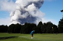 A man plays gold in Hawaii in 2018 as a huge ash plume rises behind him.