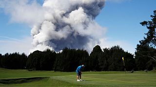  Човек играе злато в Хавай през 2018 година, до момента в който голяма пепелна бликам се издига зад него. 