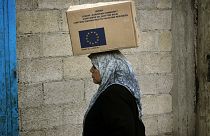 A Palestinian woman carries a box with supplies donated by the European Union at a warehouse at the Jebaliya refugee camp in the northern Gaza Strip