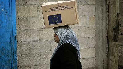 Una mujer palestina transporta una caja con suministros donados por la Unión Europea en un almacén del campo de refugiados de Jebaliya, en el norte de la Franja de Gaza.