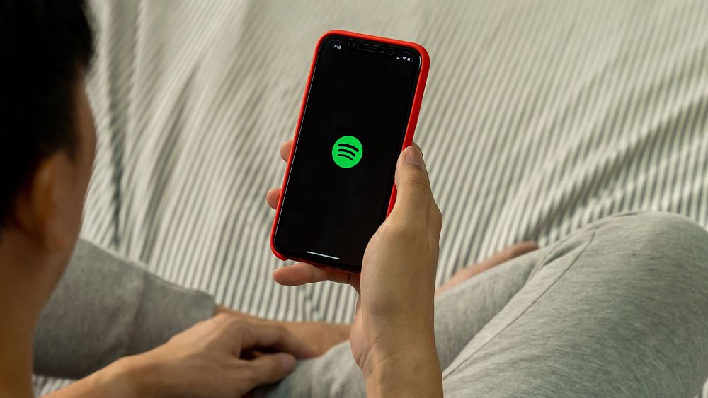 Мъж държи телефон с отворен Spotify - Авторски права: Canva От Тео Фарант