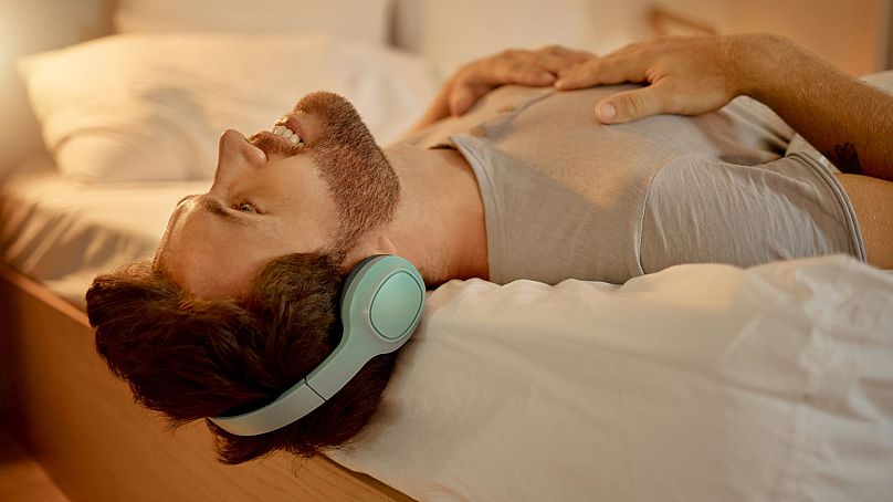 A man lying down on bed listening to music through headphones