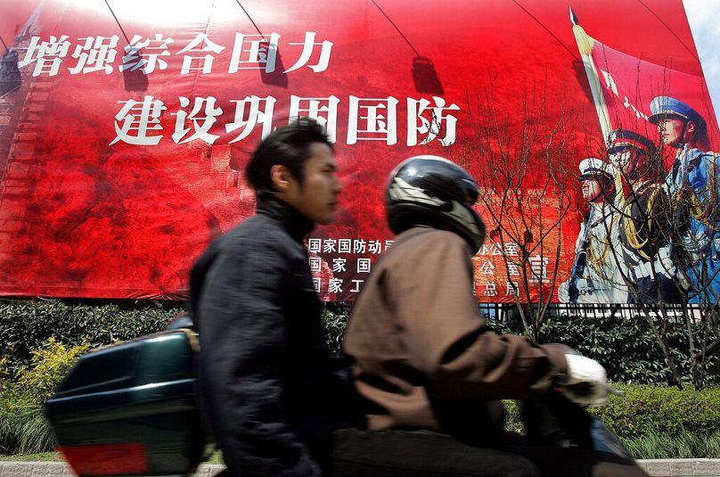 Men ride motorcycle past a government slogan in Chinese