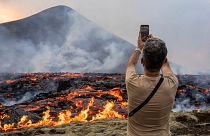 Ein Mann fotografiert, wie Lava aus einer Spalte des Vulkans Fagradalsfjall in der Nähe des Berges Litli-Hrútur austritt.