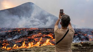 Ein Mann fotografiert, wie Lava aus einer Spalte des Vulkans Fagradalsfjall in der Nähe des Berges Litli-Hrútur austritt.
