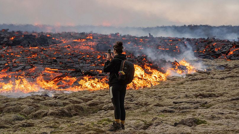 Eine Frau macht am 10. Juli 2023 ein Foto von der Lava, die aus einer Spalte des Vulkans Fagradalsfjall in der Nähe des Berges Litli-Hrútur austritt.