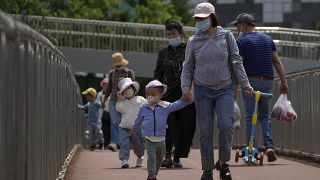 Women wearing face masks walk with masked children as they closing a pedestrian overhead bridge in Beijing, Sunday, May 21, 2023.