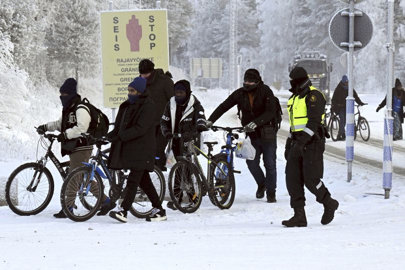 أحد حرس الحدود الفنلنديين مع مهاجرين عند المعبر الحدودي الدولي في سالا، شمال فنلندا، 21 نوفمبر 2023