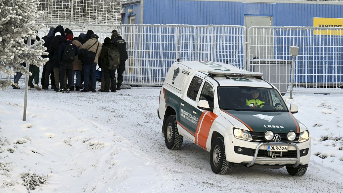 Migrant:innen und ein Fahrzeug des finnischen Grenzschutzes sind am 22. November 2023 am internationalen Grenzübergang in Salla in Nordfinnland zu sehen.