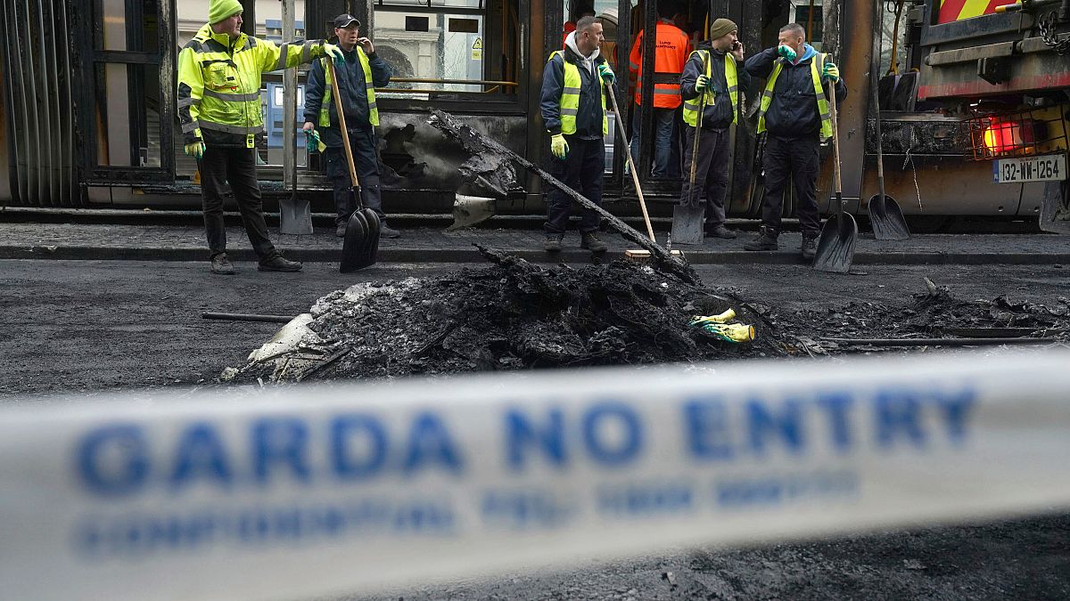 A car burns as Irish policemen stand at the scene of an attack in Dublin city centre, Thursday Nov. 23, 2023