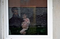 A Palestinian refugee man holds his child behind a window at a refugee centre, in Salakovac, Bosnia on Thursday