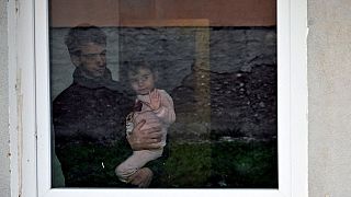 A Palestinian refugee man holds his child behind a window at a refugee centre, in Salakovac, Bosnia on Thursday