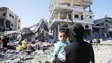 A child is seen in a woman's arms as displaced Palestinians, taking shelter in hospitals and schools, walk amid destruction as a result of Israeli attacks