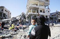 A child is seen in a woman's arms as displaced Palestinians, taking shelter in hospitals and schools, walk amid destruction as a result of Israeli attacks