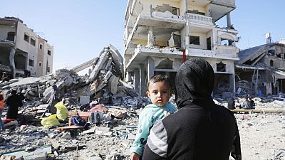A child is seen in a woman's arms as displaced Palestinians, taking shelter in hospitals and schools, walk amid destruction as a result of Israeli attacks