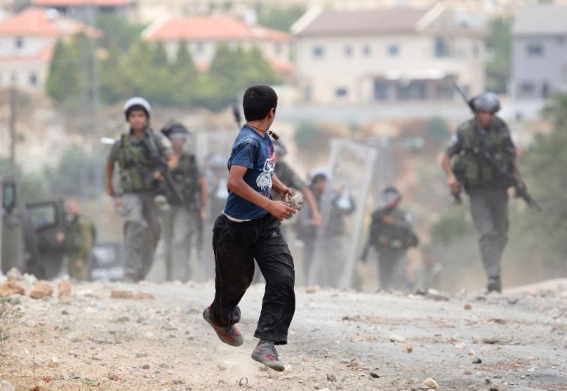 Palesztin fiú, kövekkel a kezében, izraeli katonák elől menekül Kdumim közelében, 2012-ben