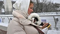 امرأة تتفحص هاتفها الذكي وهي تمسك بكلب في سترتها في كييف. 2023/11/22